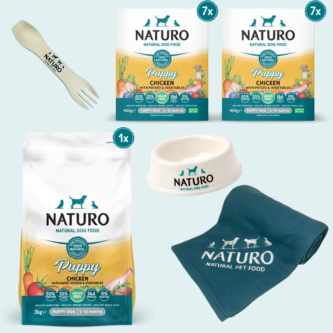 A bundle of Naturo puppy food, including a 2kg bag of grain-free chicken and sweet potato dry dog food, seven 400g trays of the same food, a biodegradable spork, a small dog bowl, and a blanket with the Naturo logo.