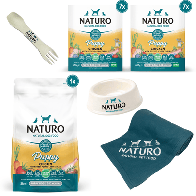 A bundle of Naturo puppy food, including a 2kg bag of grain-free chicken and sweet potato dry dog food, seven 400g trays of the same food, a biodegradable spork, a small dog bowl, and a blanket with the Naturo logo.