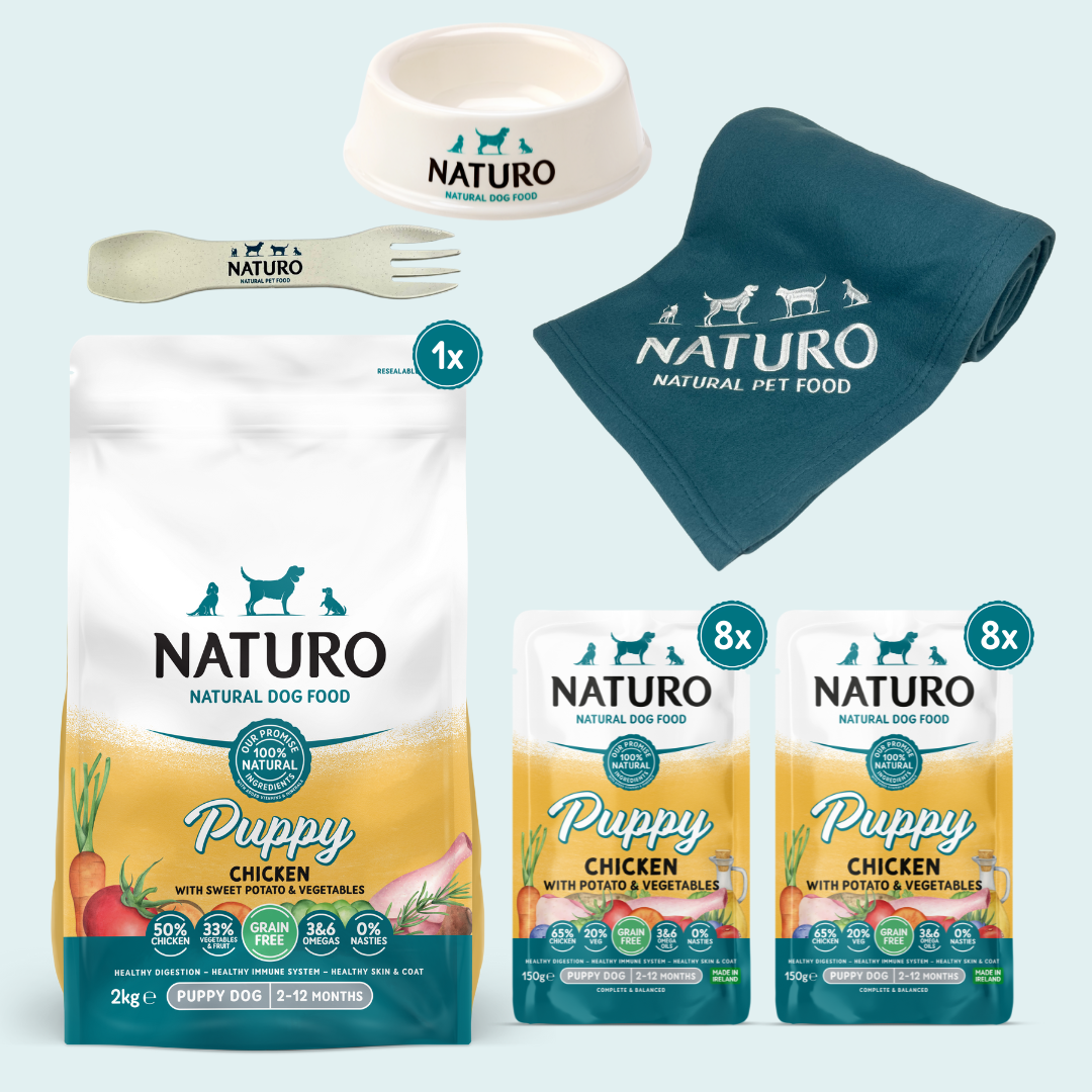 A collection of Naturo puppy dog food and accessories, including a bag of dry dog food, pouches of wet dog food, a dog bowl, a biodegradable spork, and a blanket, all branded with the Naturo logo.
