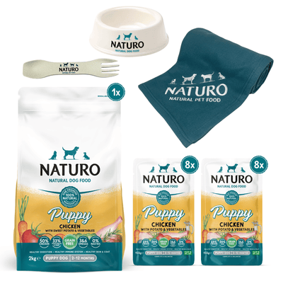 A collection of Naturo puppy dog food and accessories, including a bag of dry dog food, pouches of wet dog food, a dog bowl, a biodegradable spork, and a blanket, all branded with the Naturo logo.