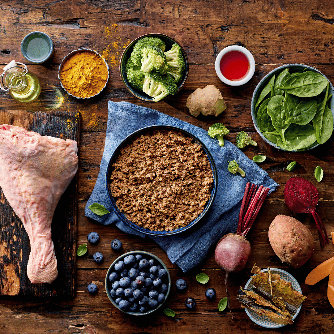 Assorted ingredients including a chicken leg, ground meat, vegetables, and spices on a wooden surface.