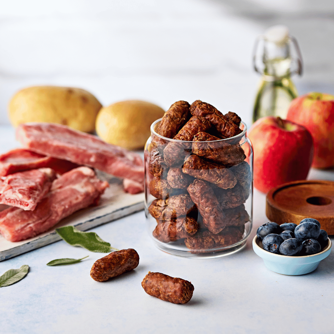 Glass jar filled with Naturo dog treats with sausages dog treats ingredients in the background